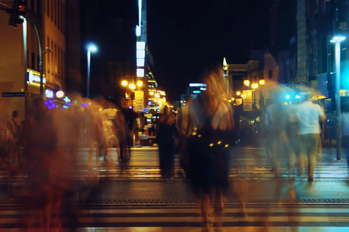 A brightly lit city street at night crowded with motion-blurred pedestrians and signage, reflecting the constant noise and distraction competing for attention online